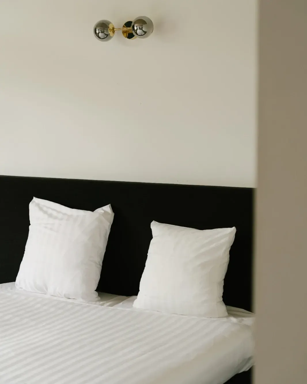 A made bed with striped linen under a brass wall light